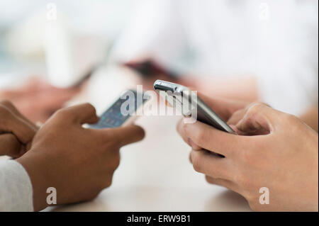 Close up of friends texting with cell phones at table Stock Photo