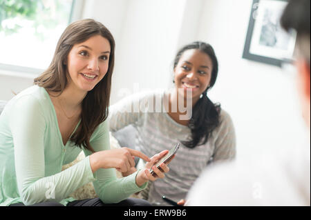 Smiling woman pointing to cell phone with friends Stock Photo