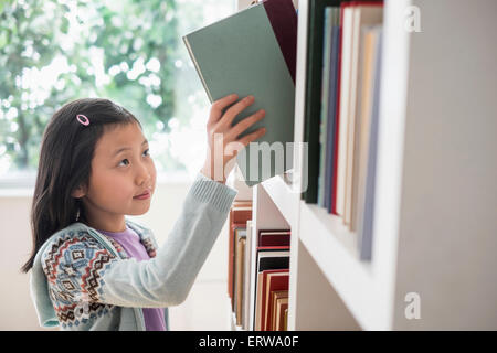 Chinese student selecting book from library bookcase Stock Photo