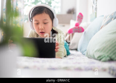 Chinese girl using digital tablet with headphones on bed Stock Photo