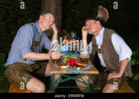 two bavarian men sitting in a park ,drinking beer and looking tired Stock Photo