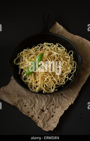 Linguine sits inside a black cast iron pan on a black surface with a crumpled brown paper bag beneath. Stock Photo