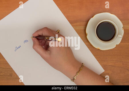 Female hand writing letter on white office paper on wooden desk. Stock Photo