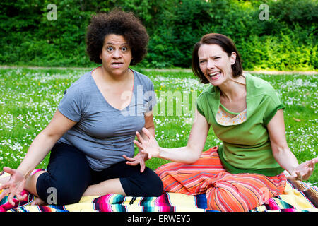 two angry women sitting on blanket in park Stock Photo