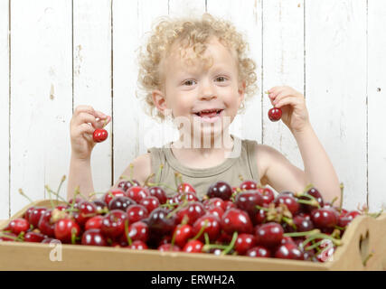 a small blond boy playing with cherries Stock Photo