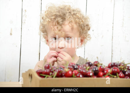 a small blond boy eating cherries Stock Photo