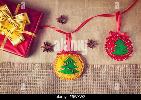 Christmas handmade toys from felt, red box with yellow bow and anise stars around on paper and sackcloth background Stock Photo