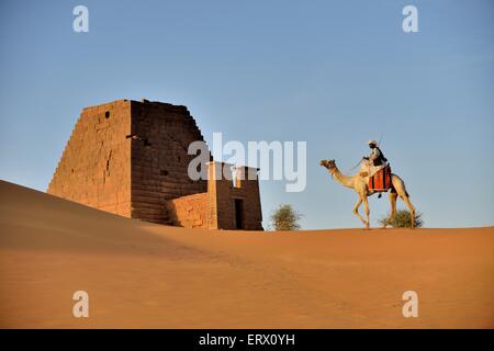Man riding a dromedar in front of a pyramid of the northern cemetery of Meroe, Nubia, Nahr an-Nil, Sudan Stock Photo