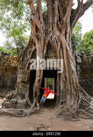 Girl at a gopuram, Strangler fig (Ficus altissima) wraps a relief, Ta Som Temple, Angkor, Siem Reap Province, Cambodia Stock Photo