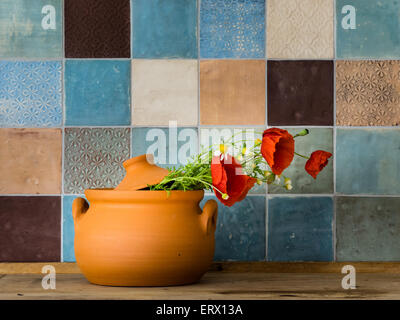 Poppies in a handmade ceramic pot in front of a colorful tiled wall in a countryside kitchen Stock Photo