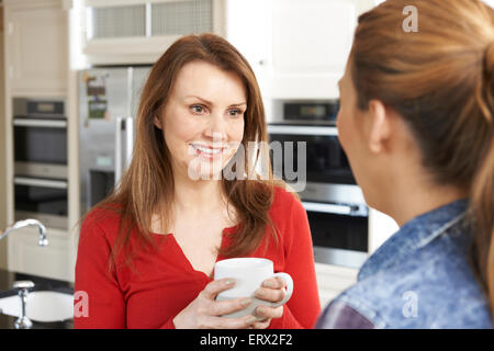 Two Mature Female Friends Talking In Kitchen Together Stock Photo