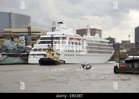 Tug moving MV Silver Cloud from her berth next to HMS Belfast on the River Thames London UK Stock Photo