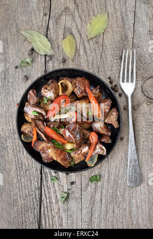 Roasted chicken liver with pepper in frying pan and fork on wooden table, top view Stock Photo