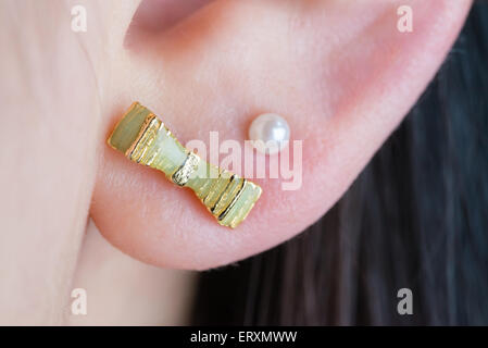 A macro shot of a green ribbon earring and white pearl earring in a girl's ear. Stock Photo