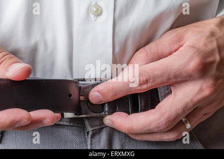 A man wearing grey pants and a white button up shirt buckling his belt. Stock Photo