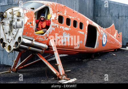 A visitor to Antarctica waves from a de Havilland Otter aircraft once used for the British Antarctic Survey that was based at Whalers Bay on Deception Island in the South Shetland Islands off the Antarctic Peninsula. In 2004 the derelict airplane was moved for safekeeping to the De Havilland Aircraft Heritage Centre in London, England. Stock Photo