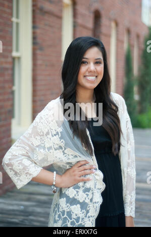 Beautiful and happy senior graduate standing in front of building wearing a dress. Stock Photo