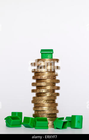 A small plastic model green house on top of a pile of pound coins in the middle of overturned houses. Housing finance concept.