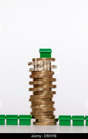 A small plastic model green house on top of a pile of pound coins in the middle of terrace of houses. Housing finance concept.