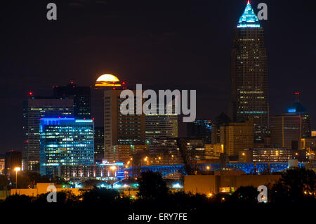 The full moon, with cloud bands, rises behind downtown buildings of Cleveland Ohio Stock Photo