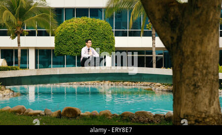 Asian businessman relaxing outside office building. The man does yoga on a bridge and smiles with eyes closed in prayer position Stock Photo