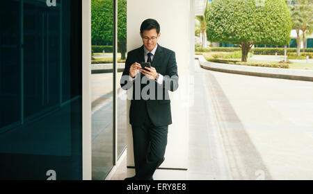 Young chinese businessman typing note on mobile phone. The man uses a digital pen to write on the device and smiles Stock Photo