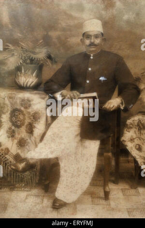 Old vintage antique 1900s black and white studio photograph of Indian man wearing sherwani pagdi sitting in a chair , india , asia Stock Photo