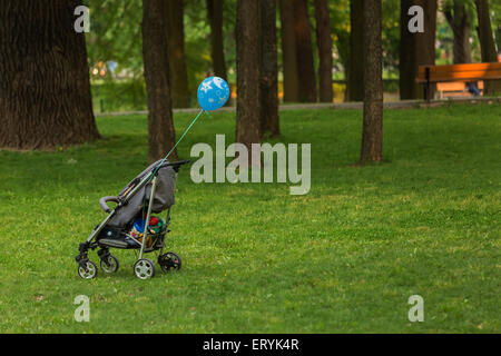 Baby trolley isolated in a park with blue balloon Stock Photo