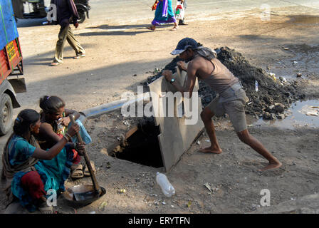 Man closing sewage drainage pipe cover after cleaning , Bombay ,  Mumbai ; Maharashtra ; India , Asia , Indian , Asian Stock Photo