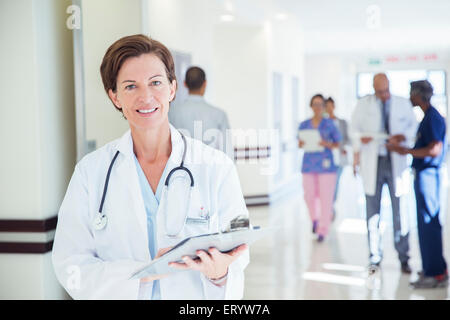 Portrait of confident doctor with clipboard in hospital corridor Stock Photo