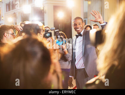 Celebrity waving for paparazzi with cameras at event Stock Photo
