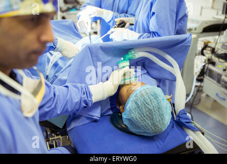 Anesthesiologist holding oxygen mask over patient’s face in operating room Stock Photo