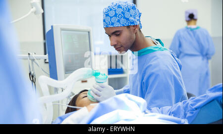 Anesthesiologist holding oxygen mask over patient’s face in operating room Stock Photo