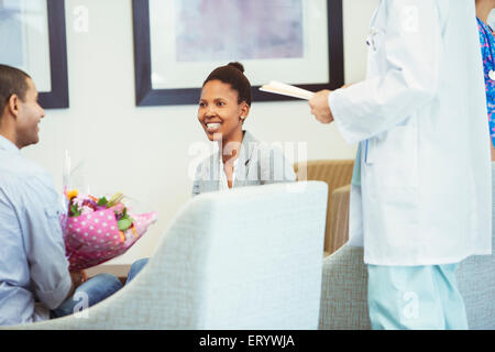 Doctor meeting with smiling couple in hospital waiting room Stock Photo