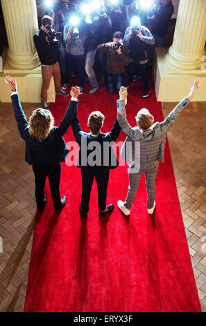 Celebrities holding hands with arms raised for paparazzi photographers at red carpet event Stock Photo