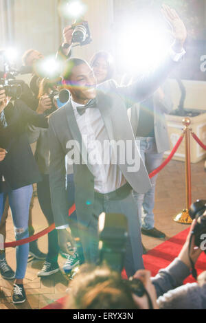 Smiling celebrity waving and being photographed by paparazzi photographers Stock Photo