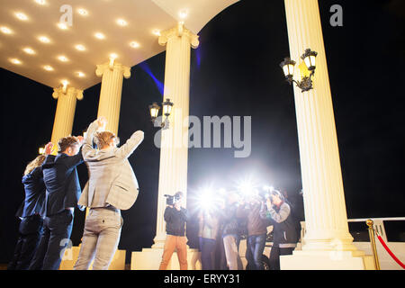 Celebrities posing with arms raised for paparazzi photographers at event Stock Photo