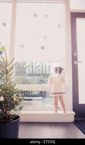 Curious girl on window ledge below Christmas ornaments Stock Photo