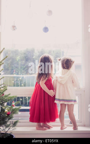 Girls on window ledge below Christmas ornaments Stock Photo