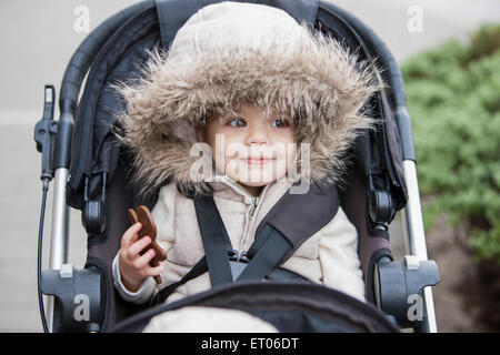 Smiling girl in fur hood riding in stroller Stock Photo