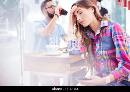 Tired woman with head in hands at cafe Stock Photo