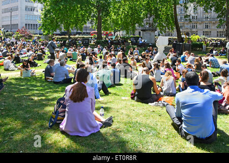 London people in Cavendish Square gardens mainly office and shop workers sitting on grass at lunch time break on a warm summer day London England UK Stock Photo