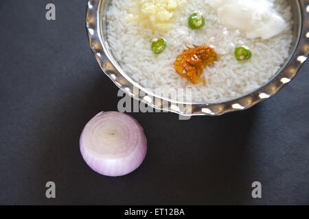 Indian lunch pakhala rice pickle mash potato with chillies and yoghurt in steel bowl onion black background Stock Photo