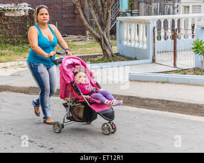 A thirty something Cuban mother walks, pushing her young son in his stroller in Santiago de Cuba. Stock Photo