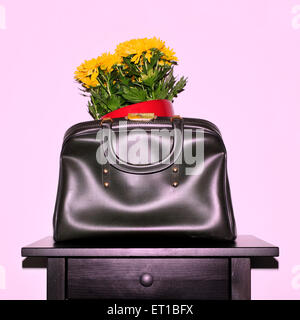 yellow chrysanthemum flowers in a vintage leather bag on a black table, with a retro snapshot effect Stock Photo