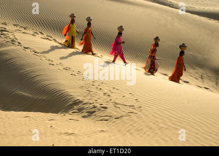Women with earthen pots on head walking on desert of khuhri ; Jaisalmer ; Rajasthan ; India