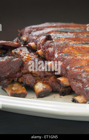 Pork ribs sit atop a white plate after being seared on the grill and then slow roasted in the oven. Stock Photo