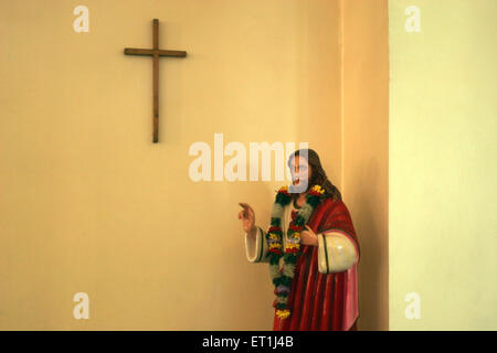 Statue of Jesus in church with cross on wall ; Pune ; Maharashtra ; India Stock Photo