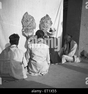 Men sitting behind cloth screen light thrown manipulate leather flat puppet's shadow puppet play ; Hallare village ; Mysore Stock Photo