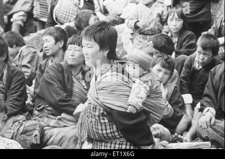 Bhutanese mother and child walk past the crowd at festival at Paro ; Bhutan Stock Photo